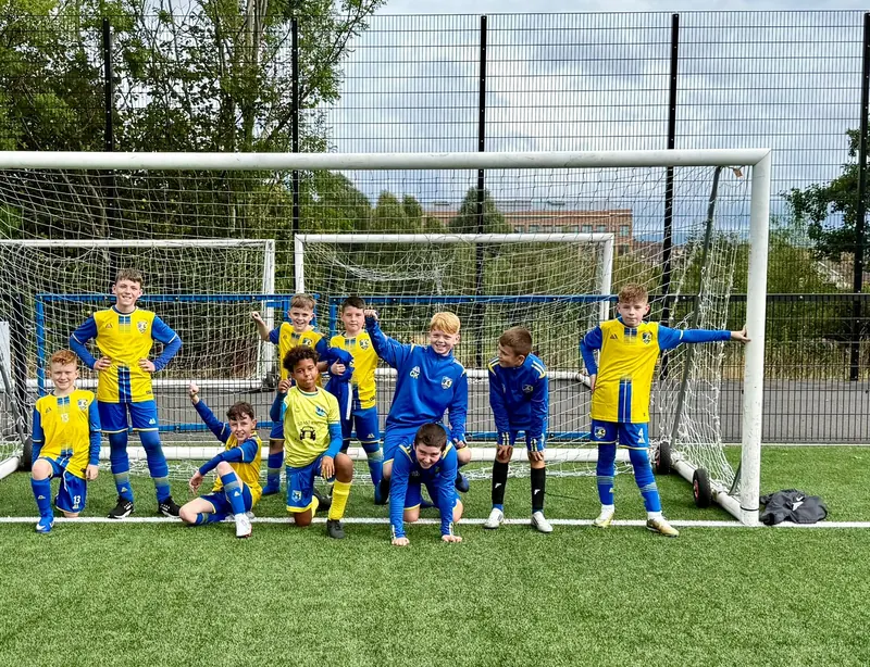 A squad in yellow and blue kit striking fun poses in a goal